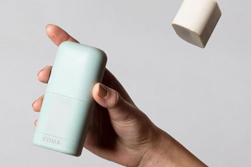 Hand holding a refillable Kiima deodorant, with two solid refills floating above against a neutral background.